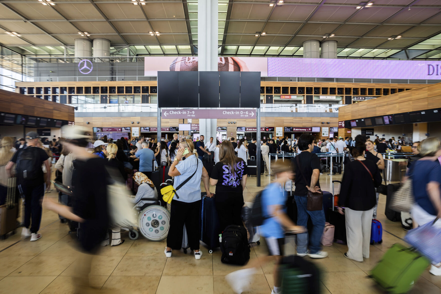 Numerous passengers wait in front of a black display board at the capital