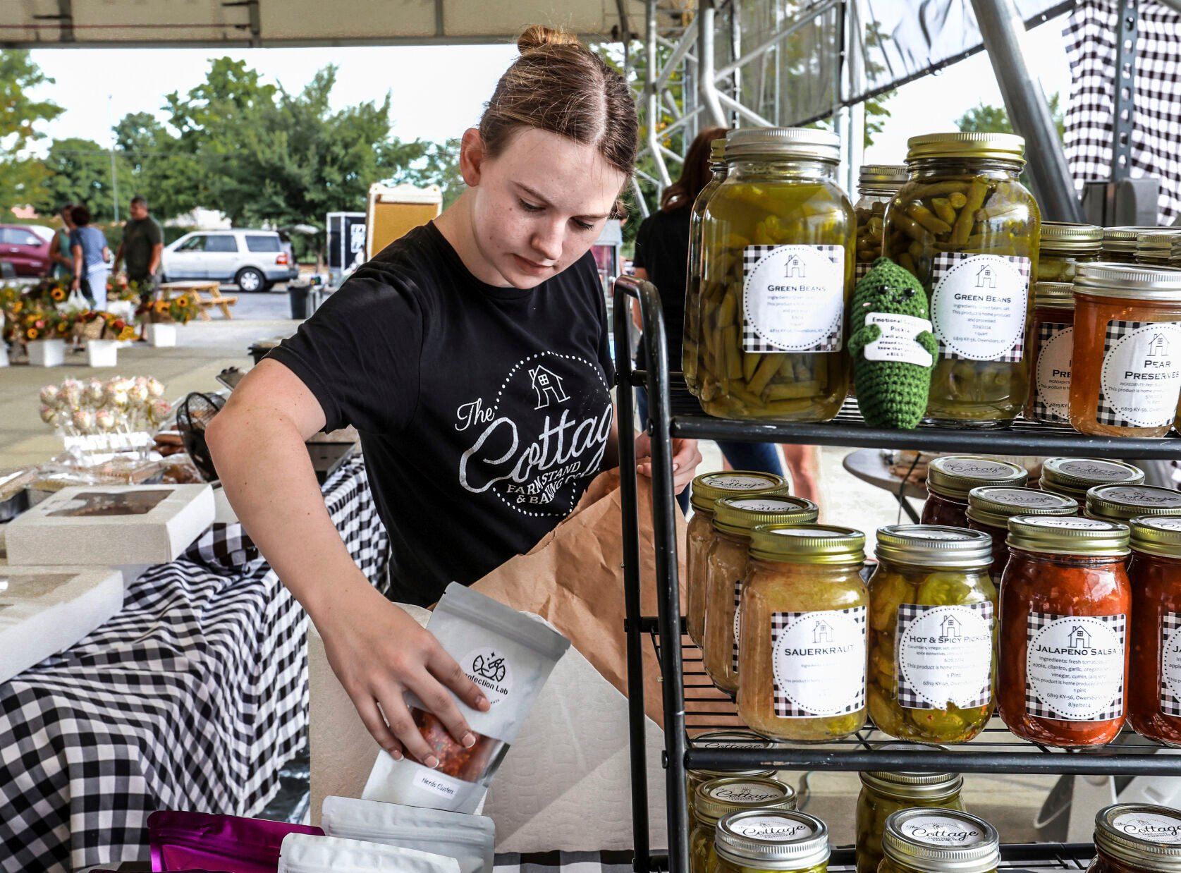 FILE - Lexia Smith stocks product while working in The Cottage Farm Stand & Baking Co. vendor booth set up at the Owensboro Regional Farmers