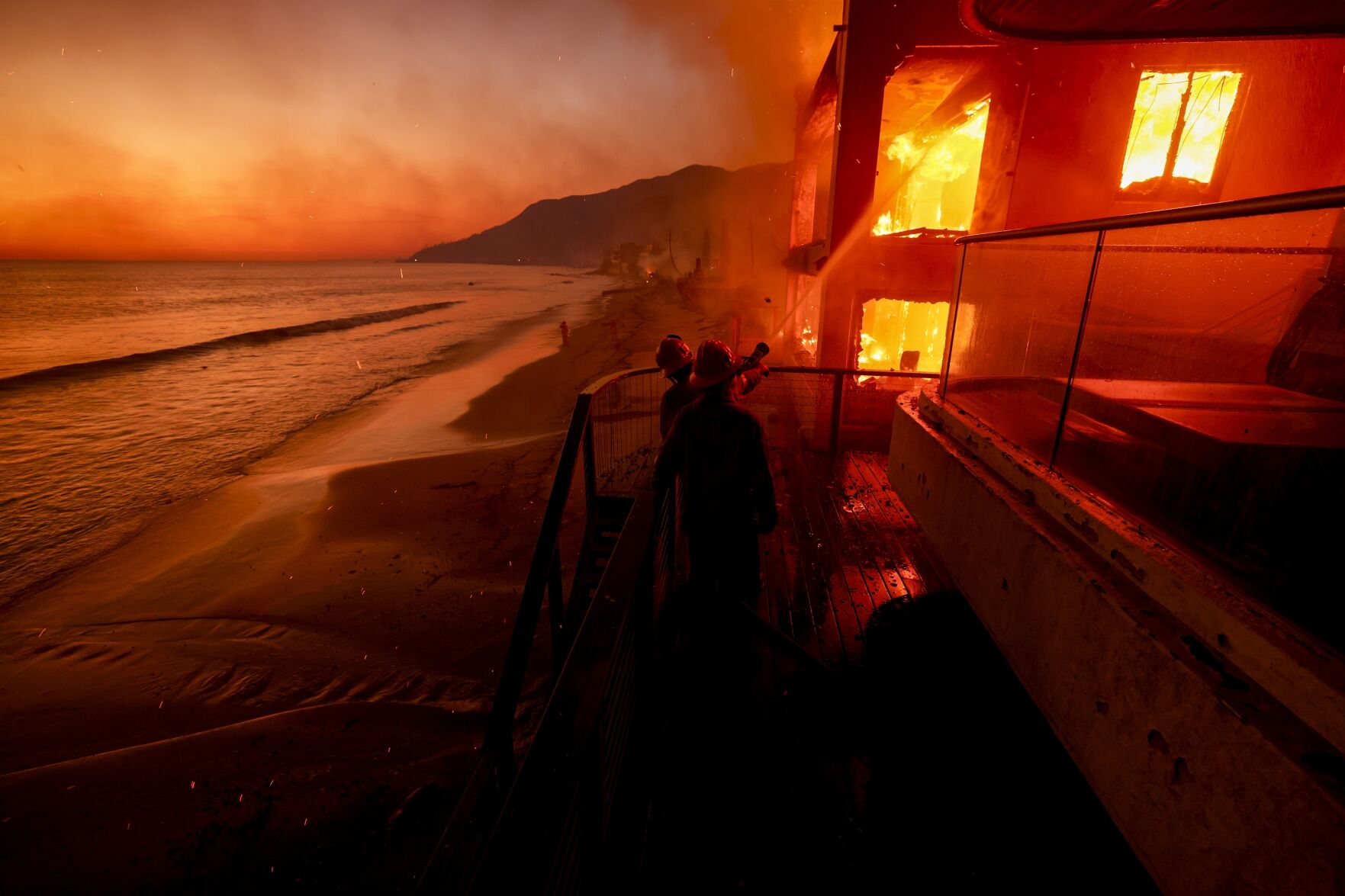 <p>Firefighters work from a deck as the Palisades Fire burns a beachfront property Jan. 8, 2025, in Malibu, Calif. (AP Photo/Etienne Laurent)</p>   PHOTO CREDIT: Etienne Laurent 